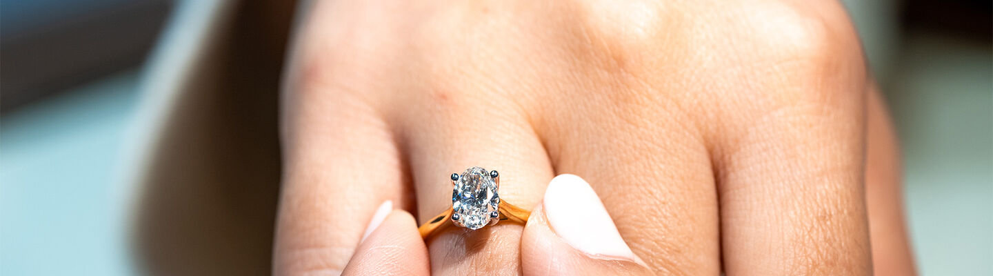 Close-up of oval diamond engagement ring in yellow gold on hand, showcasing sparkle and fine claw setting